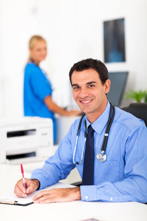 Attractive male doctor smiling and writing with a red pen and chart